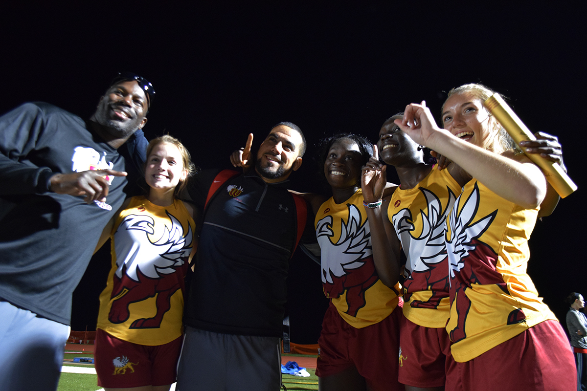 The 4x400 meter relay team and two of their coaches laugh while taking pictures.