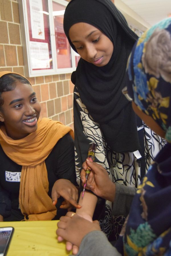 Freshman Roda Jama discusses with sophomore Ruweyda Hassan, while Hassan prepares to put a henna on freshman Sumaiya Mohamuds wrist.