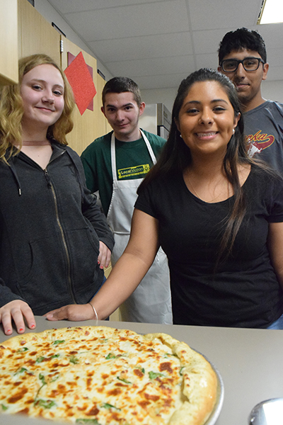 Pictured from left to right, freshman Monica Riley, sophomore Michael Bratton and seniors Hailey Gloria and Angel Chacon smile in appreciation after pulling their chicken alfredo pizza out of the oven. 